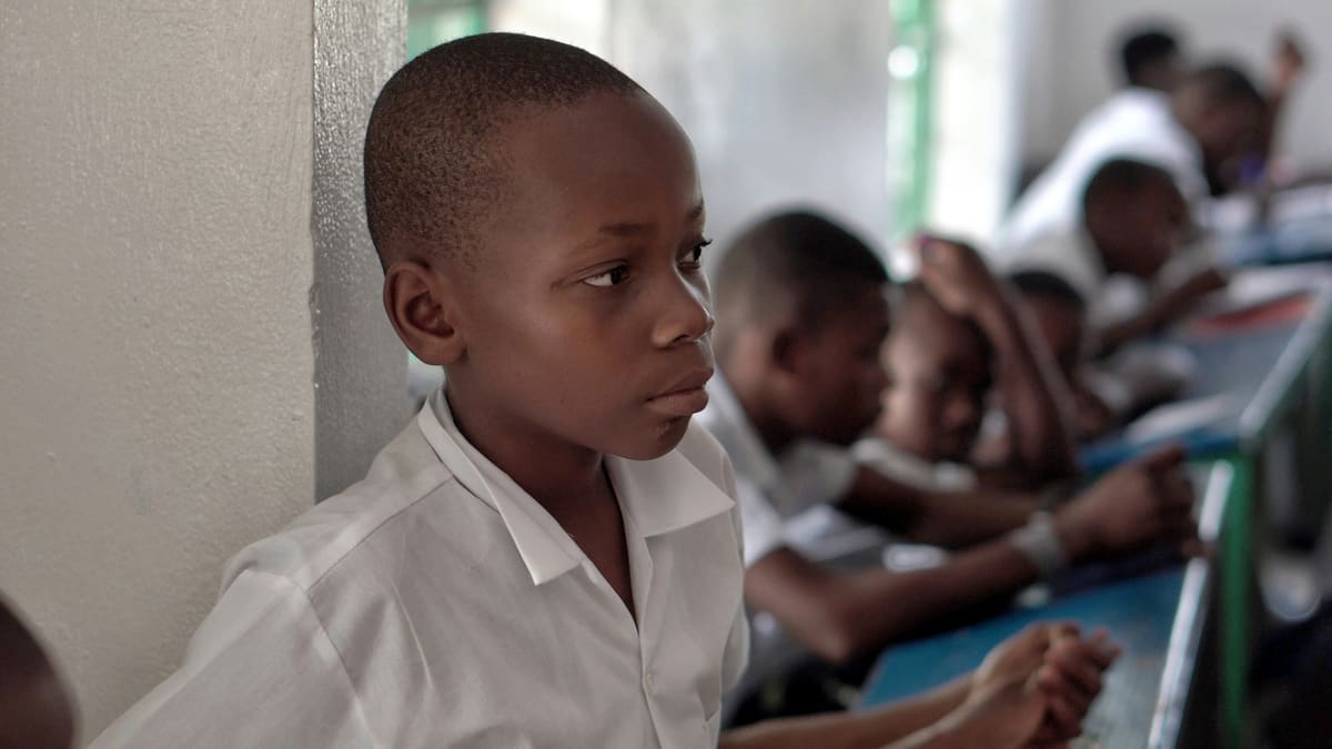 A learner in class alongside classmates writing in their notebooks
